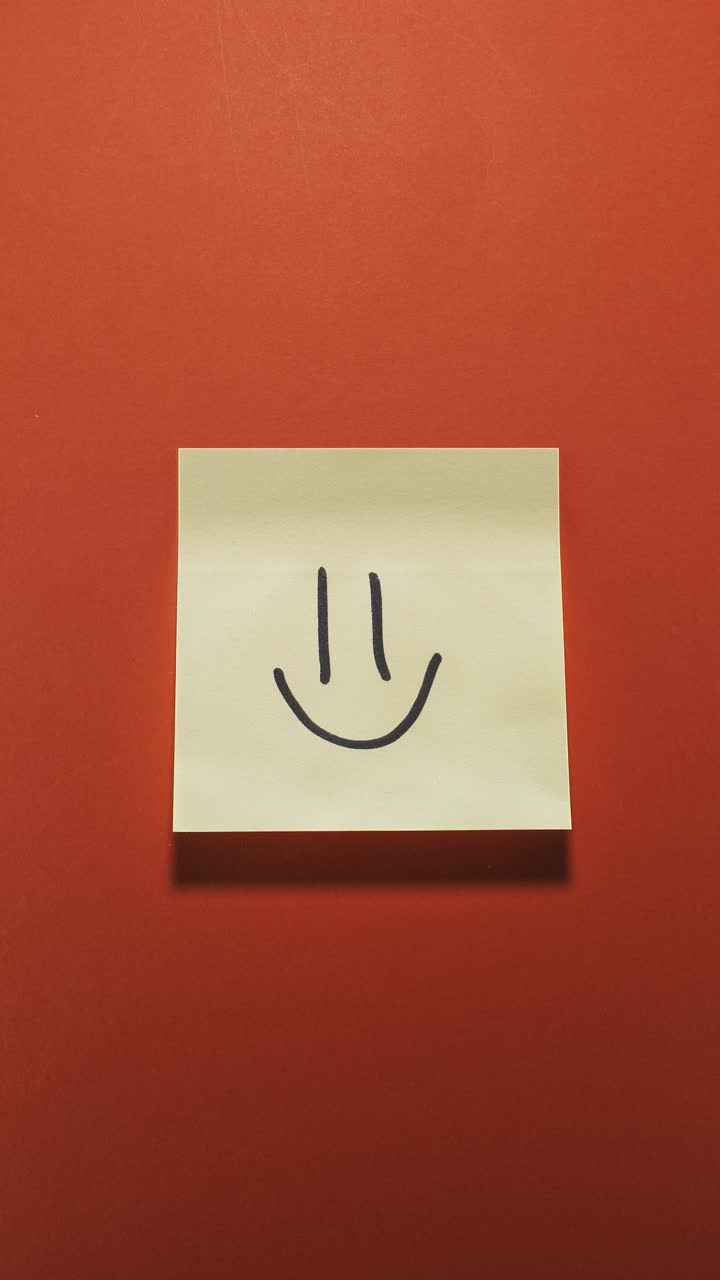 Hands posting Smiley sticky note on orange wall, symbolizing positivity