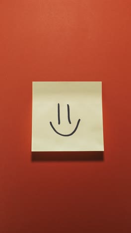 hands posting smiley sticky note on orange wall, symbolizing positivity