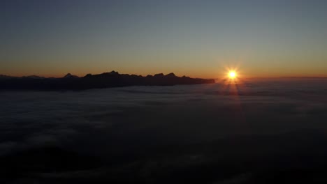 flying high and fast in reverse over sea of clouds at sunset, the alps in the background - switzerland