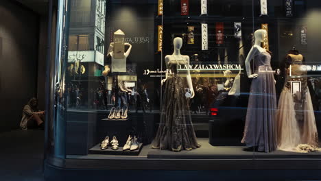 woman sits beside a luxury fashion storefront at night