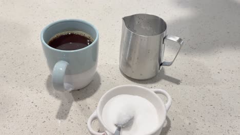 a hand adds sugar to a coffee cup on a kitchen counter, creating a serene morning routine atmosphere