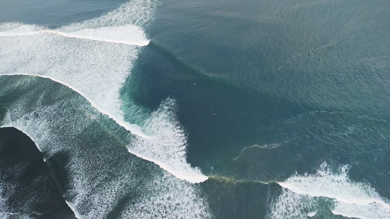 Balian surfers beach with blue green waves swelling along the shoreline with tiny surfers dwarfed by the swell