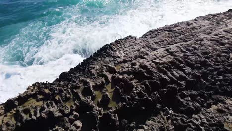 Powerful ocean waves crash against sharp volcanic rock cliffs along the Hawaiian coast, showcasing the raw beauty and force of nature.