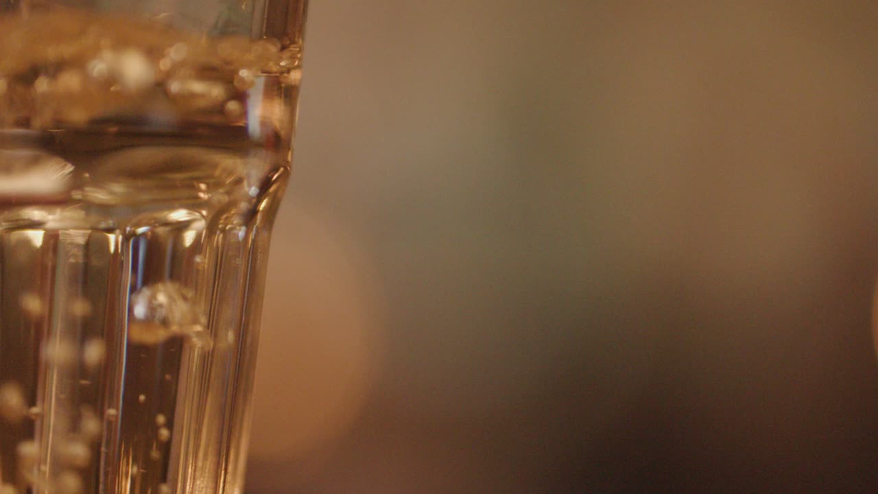 A close-up shot of water being poured into a clear glass with warm, blurred restaurant lights in the background, creating a cozy nighttime ambiance