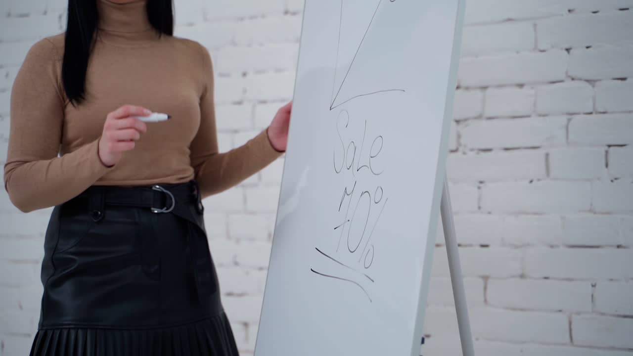 Young business woman writes on a board with a marker. Dark-haired woman writing on a white board the word sale. Slow motion. Business concept.