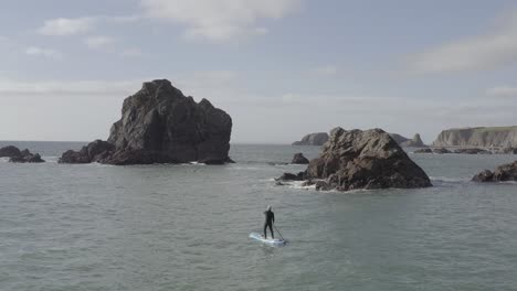 aerial follows sup paddleboard man on choppy ocean near jagged islet