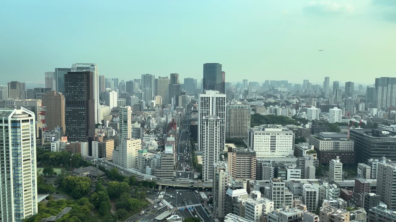 vista estática de ángulo ancho de tokio desde un edificio mirando hacia el sur en un caluroso día de verano nebuloso con un avión volando en el cielo