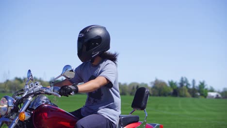 man rides a red motorcycle down a farm road in the summer wearing a helmet with a field in the background