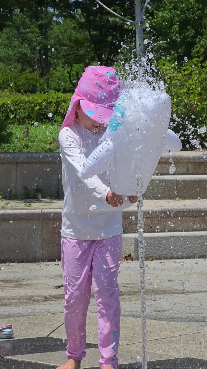 Little girl splashing water at a park fountain in Seoul on a hot summer day, dressed in sun-protective swimwear and hat