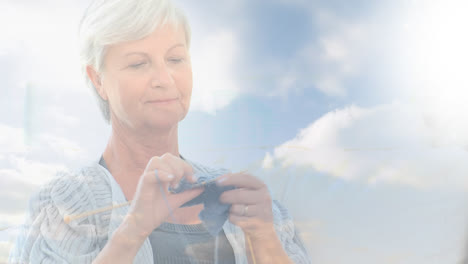 Animation-of-glowing-light-over-happy-senior-woman-knitting