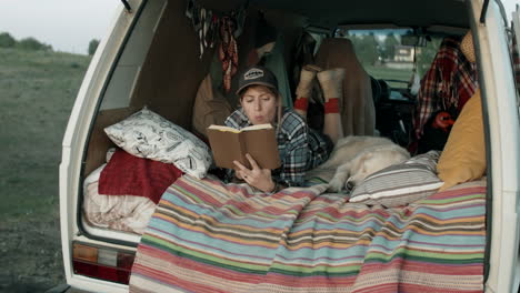 woman lying in van with dog and reading book