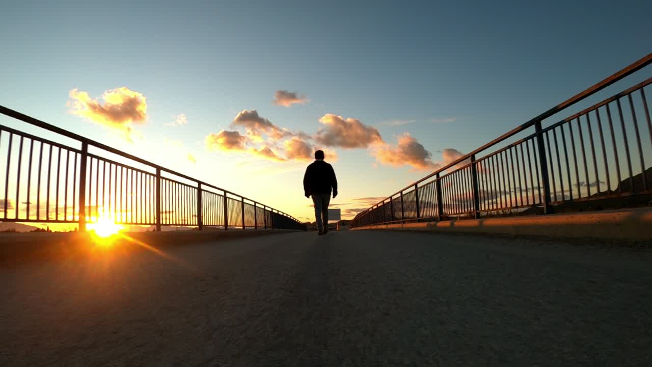silueta de hombre caminando por un puente al atardecer