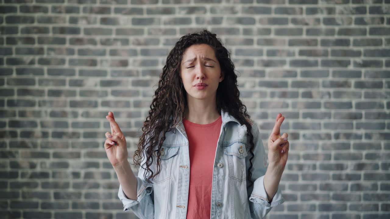 Woman Fingers Crossed in Front of Brick Wall