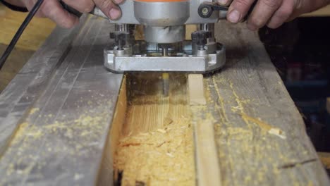 close up of carpenters hands working on piece of wood with router machine on workbench