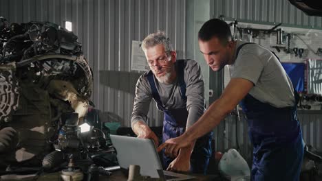 automotive technicians working on a car engine with laptop