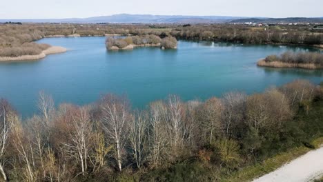 Luftüberflug,-Leerer-Weg-Und-Blattlose-Bäume-Am-Rande-Des-Wassers-In-Der-Antiken-Lagune-Von-Antela,-Areeiras-Da-Limia-In-Xinzo-De-Limia,-Ourense,-Galizien,-Spanien