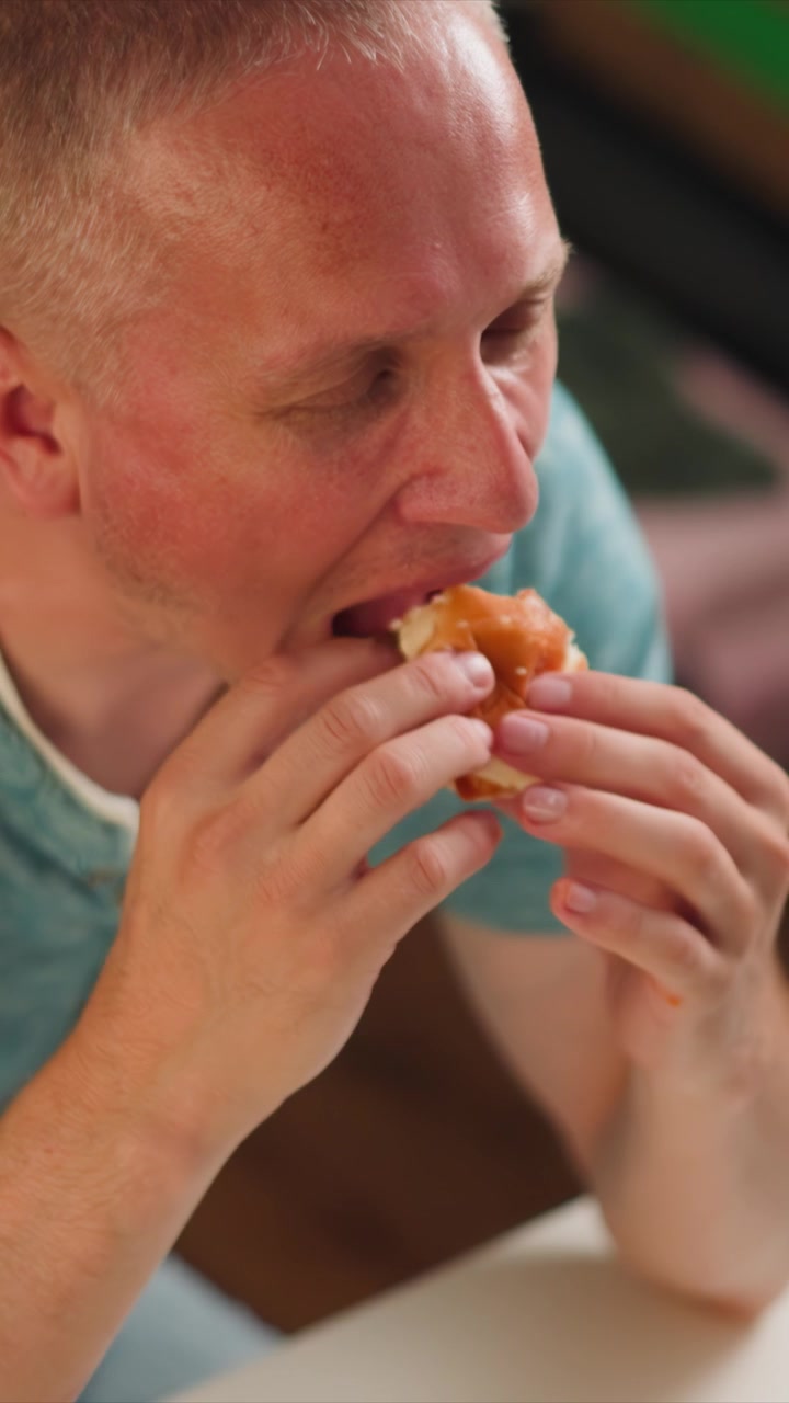 Close up of man holding partially eaten pastry with visible filling. Hands manipulate food item focusing on texture and detail. Soft indoor lighting highlights subject and object in casual