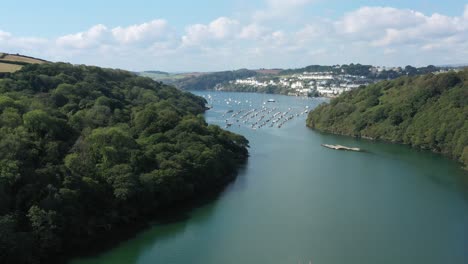 dramatic wide rising aerial reveal from paddle boarders on the river fowey, to reveal the cornish towns of fowey and polruan on the coast of cornwall, uk