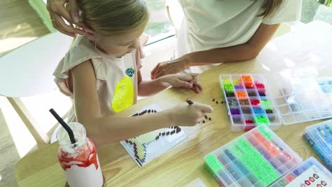 mother and daughter doing beading craft in a cafe