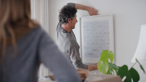 pareja feliz mudándose a una nueva casa colgando fotos en la pared decorando la casa disfrutando del trabajo en equipo 4k