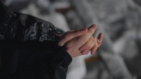 top down view of man rubbing hands together to stay warm during cold night outdoors, wearing patterned jacket and ring, surrounded by soft focus snowy background