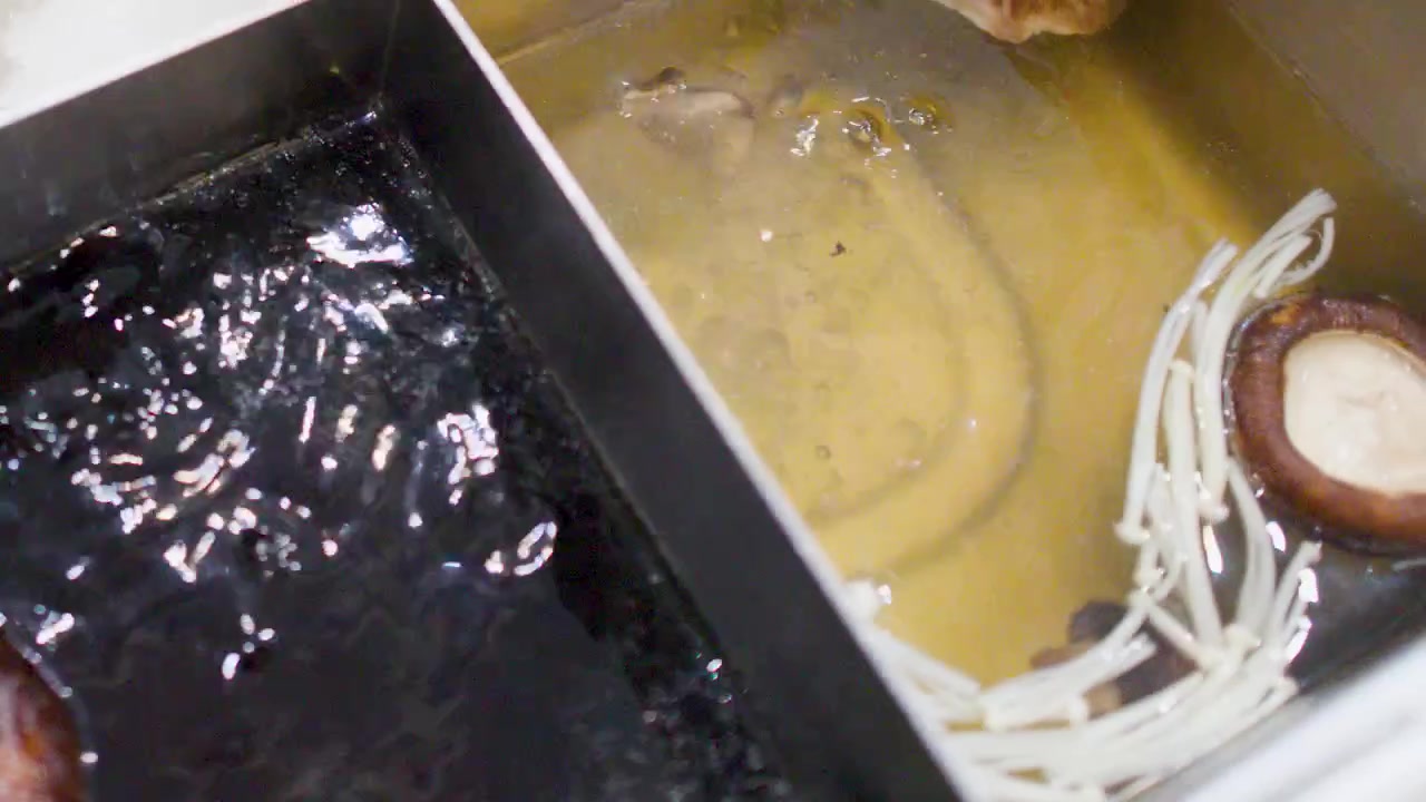 Close-up of boiling dark sukiyaki broth and clear soup in a divided stainless steel pot