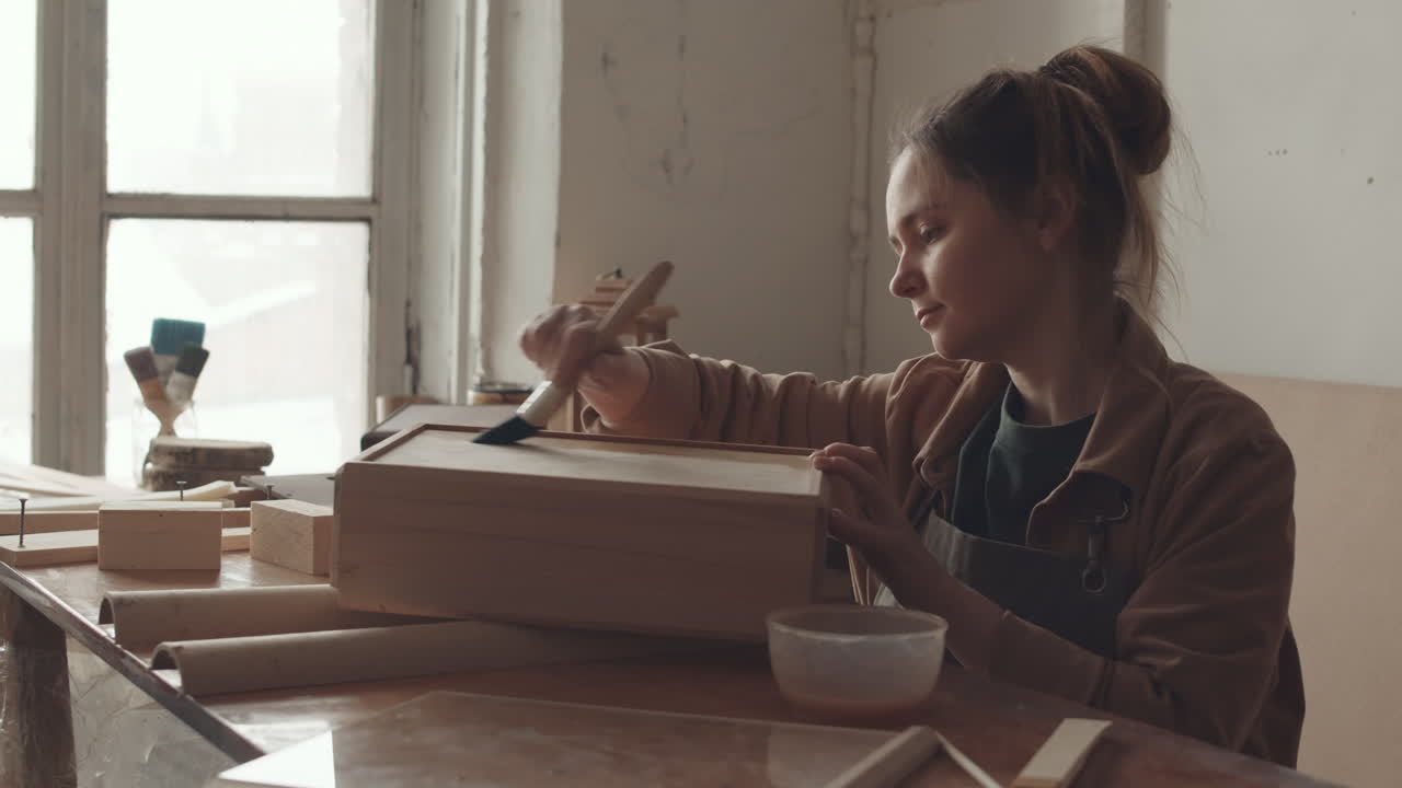 Jonge vrouw brengt beschermende vernis aan op een houten handwerkproduct
