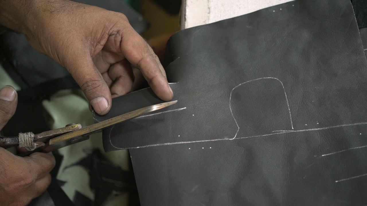 Closeup Of Sweat Shop Worker Cutting Leather With Scissors In Manufacturing Factory