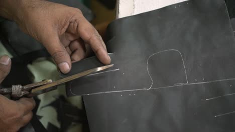 closeup of sweat shop worker cutting leather with scissors in manufacturing factory