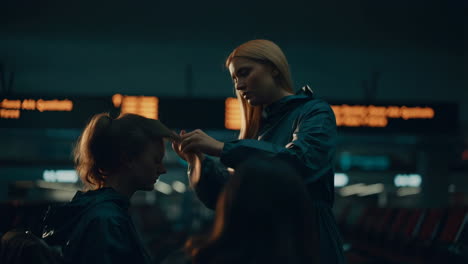 Woman styling another woman&#039;s hair in a public terminal