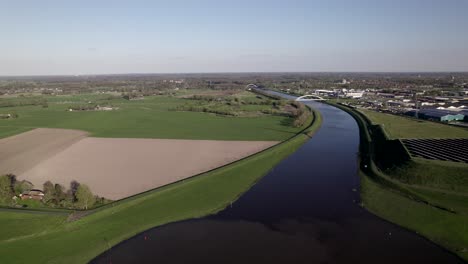 Fliegen-Entlang-Sonnenkollektoren-Mit-Schatten-Der-Sich-Bewegenden-Rotorblätter-Einer-Windkraftanlage-über-Dem-Twentekanal