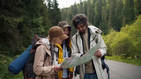 a trio of tourists get lost and are looking at a map to figure out where to go next. people in hiking clothes sort out where to have next in mountainous terrain