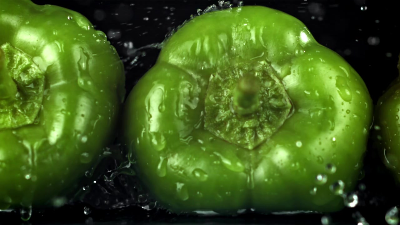 Opspattend water op verse groene paprika's in slow motion