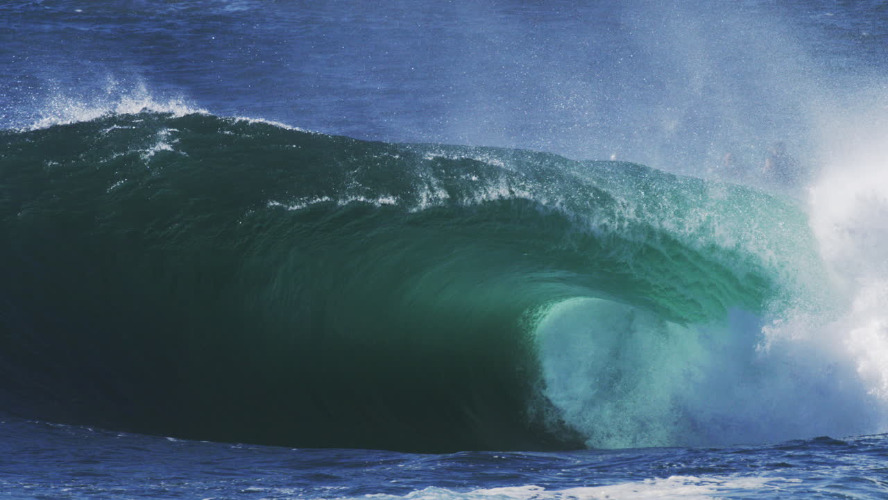 Blue wave barrels tightly with glowing mist and dramatic surface texture in motion