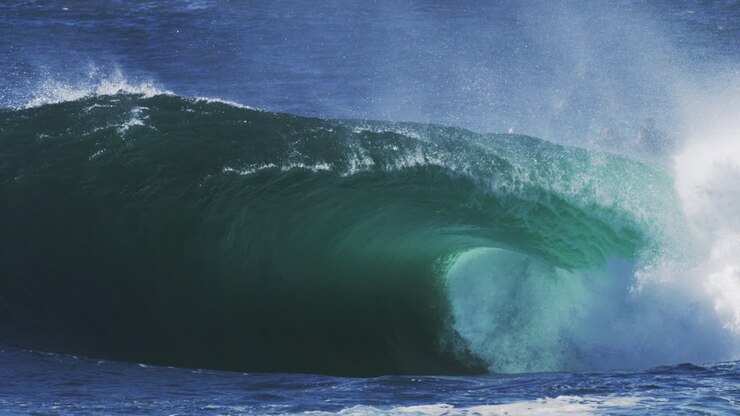Blue wave barrels tightly with glowing mist and dramatic surface texture in motion