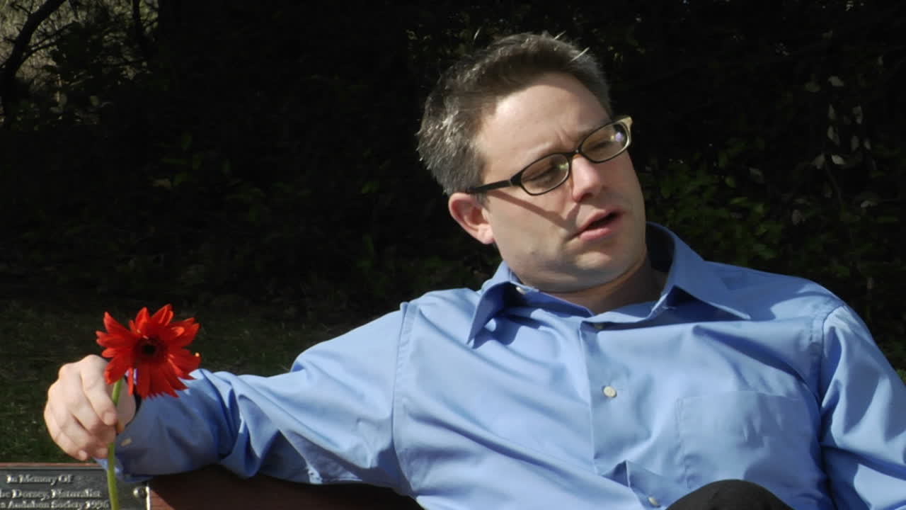 bir adam iki çiçek tutarken parkta tek başına oturuyor