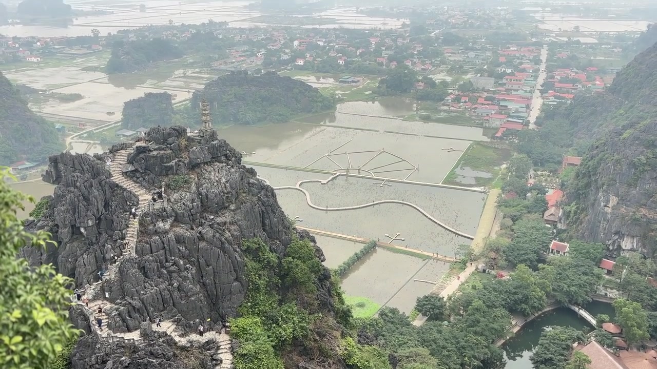 Góc nhìn từ trên cao của đỉnh núi đá vôi với cầu thang đá phía trên những cánh đồng ngập nước, thể hiện các khối đá vôi, lối đi quanh co và phong cảnh nông thôn ở Ninh Bình, Việt Nam