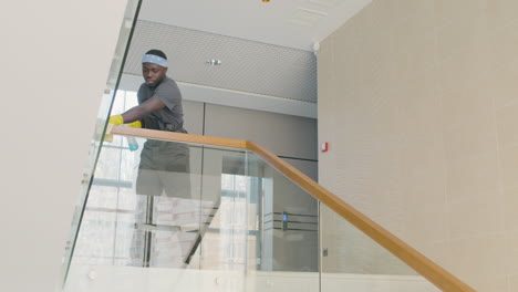 bottom view of cleaning man wearing gloves cleaning stair railing inside an office building