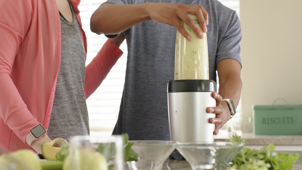 Pasangan menyiapkan minuman hijau di meja dapur, meletakkan wadah blender dan menahannya saat memblender