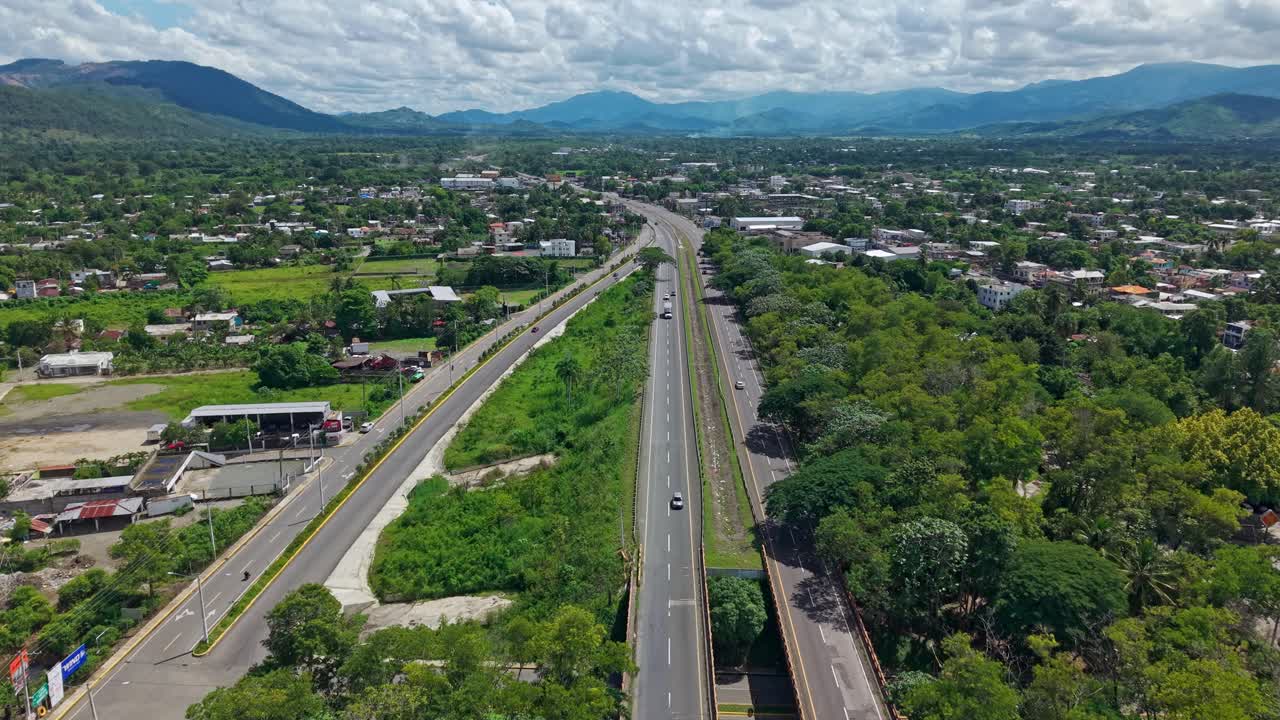 Autopista Duarte highway near Bonao, residential area and mountain landscape in background, Dominican Republic. Aerial forward