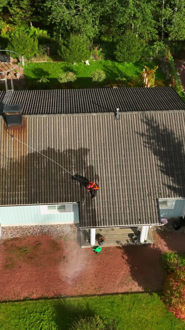 Vertical drone shot tilting toward a woman washing a house roof, autumn day