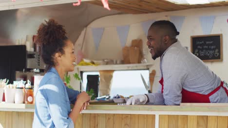 happy african american male food truck owner talking over counter to smiling female customer