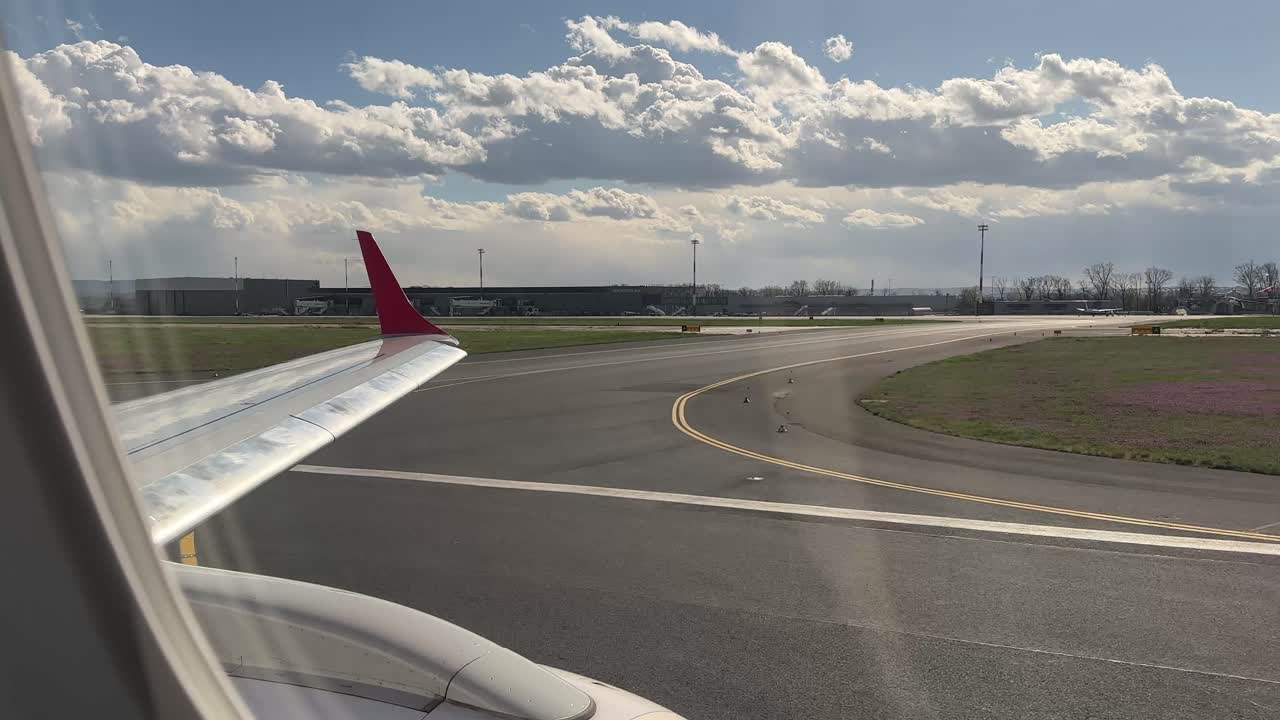 Blick aus einem Flugzeugfenster während des Starts vom internationalen Flughafen Iași, Rumänien. Der Flugzeugflügel und die Startbahn sind sichtbar, während das Flugzeug beschleunigt, mit Flughafengebäuden und Himmel