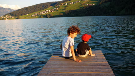 two boys sitting on a pier at a scenic lake during sunset