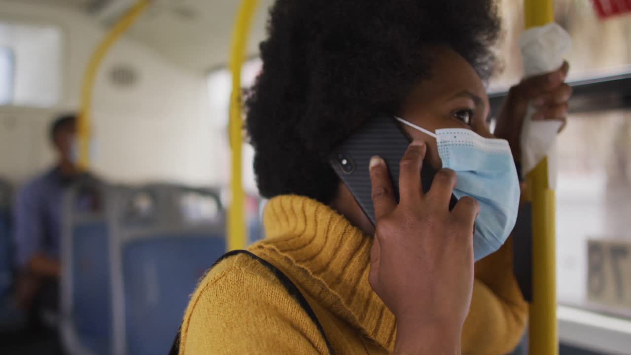 African american businesswoman with face mask talking on smartphone and standing in bus
