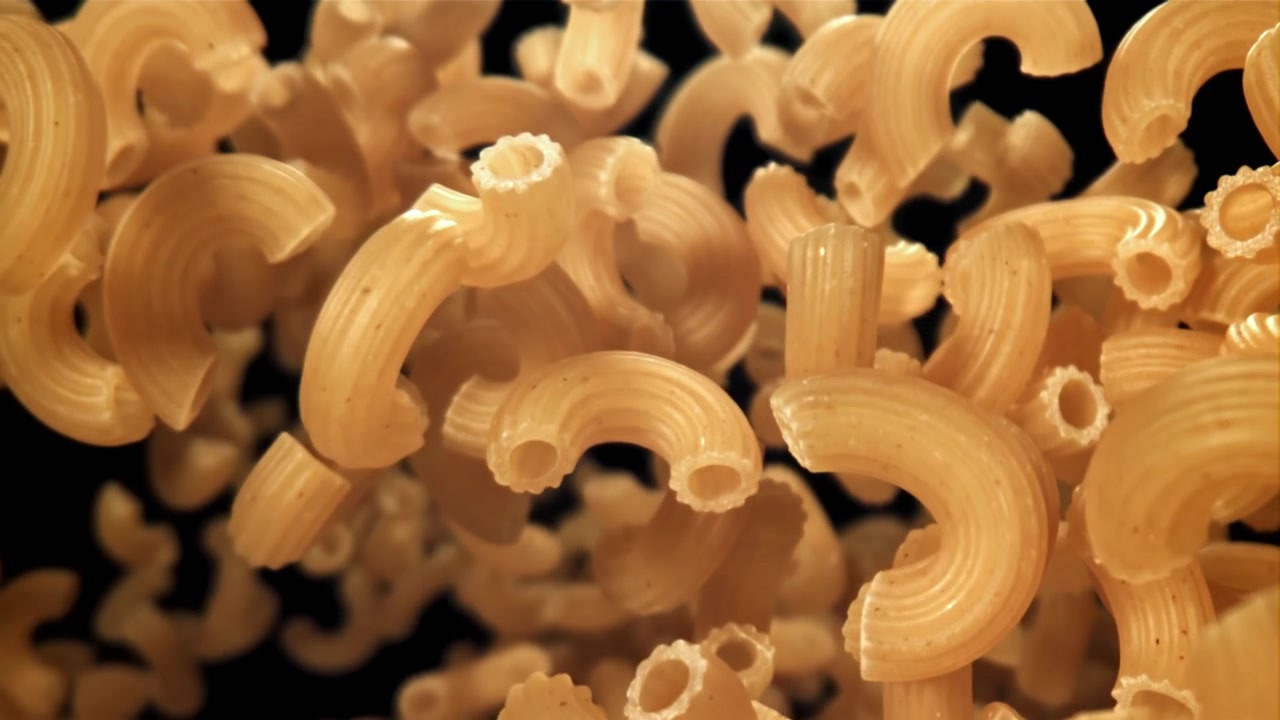 Pasta maccheroni secca che cade al rallentatore su sfondo nero.