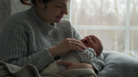 mother and yawning newborn sit by window at home