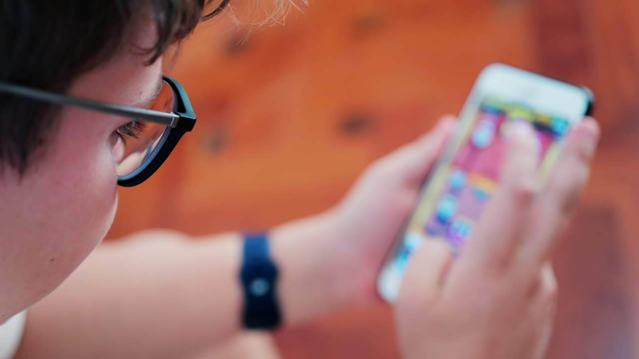 Over-the-shoulder close-up of a kid with glasses playing on a smartphone indoors