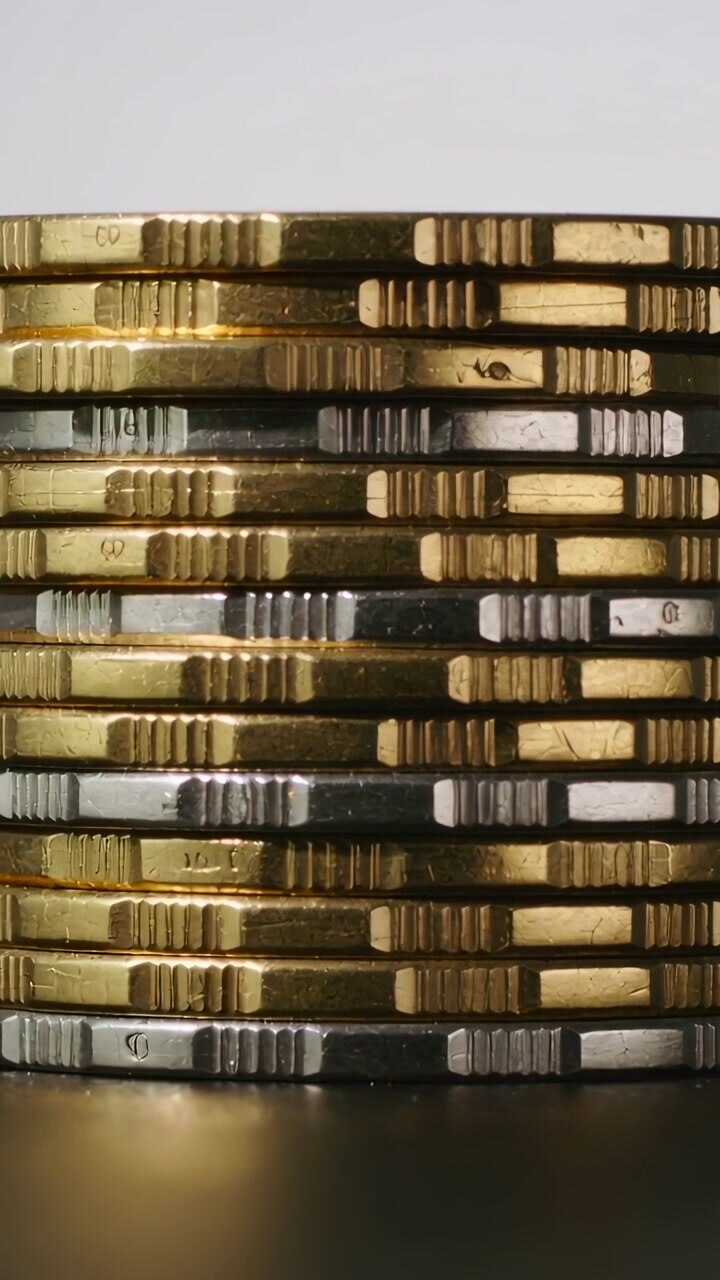 Vertical video: Zooming camera tightening around stacked metallic coins on dark table for edges