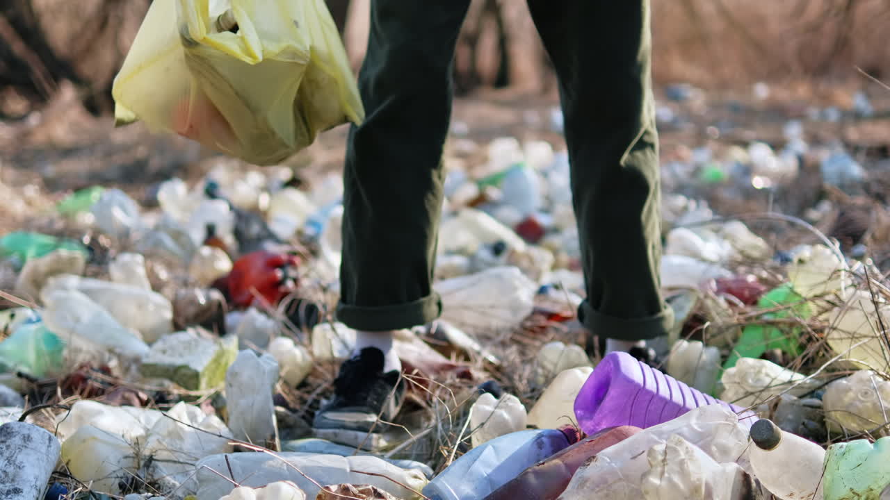 Man collecting scattered plastic bottles from the ground in the nature